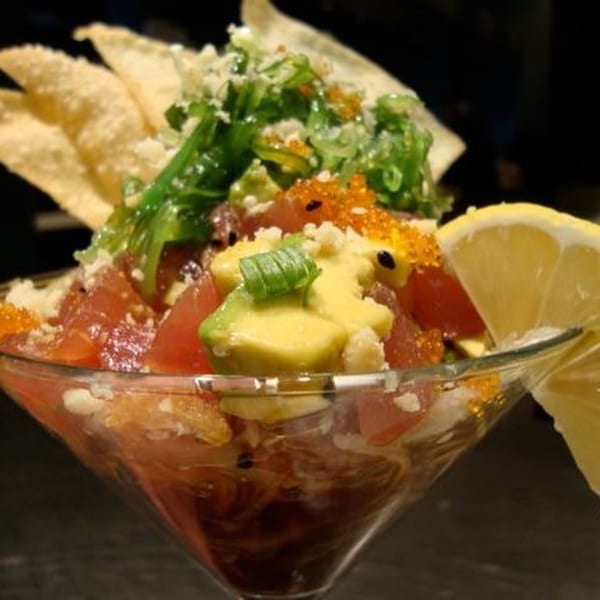 A martini glass filled with tuna poke, avocado, green onions, roe, and tortilla chips.