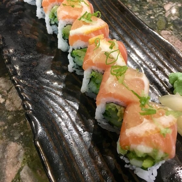A row of salmon and avocado sushi rolls topped with green onions on a dark, textured plate.