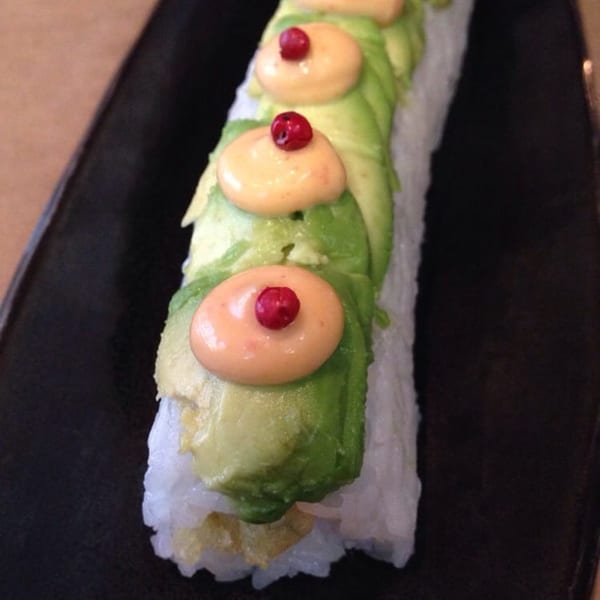 Happy Sumo sushi roll with avocado, creamy sauce, and red berries on a black plate.