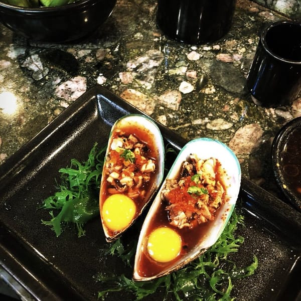 Two baked mussels with quail eggs and roe on a black plate with seaweed at The Happy Sumo.